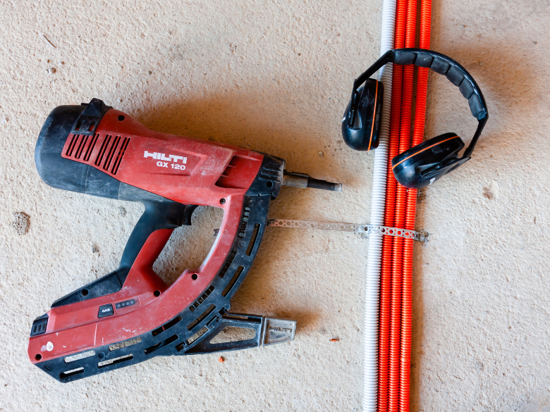 nail gun on ground beside a ruler and earmuffs