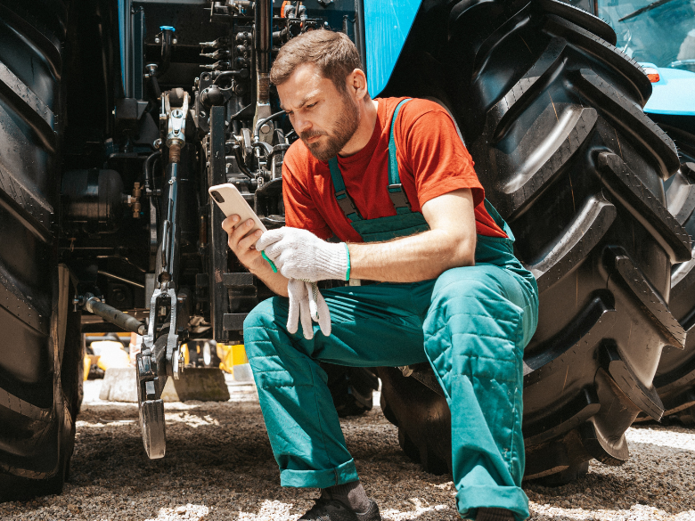 Worker using phone for H&S by tractor